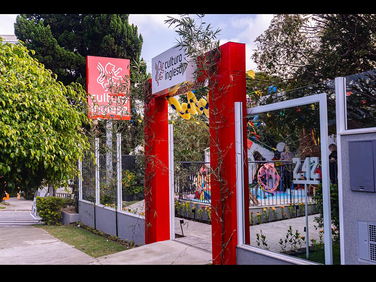 Fachada da Cultura Inglesa Taubaté, com pórtico vermelho da marca, placa, portão e jardim