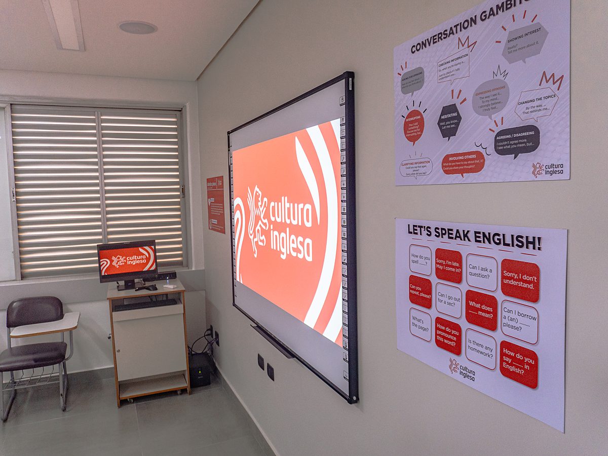Sala da unidade Taubaté com tela de projeção exibindo a marca Cultura Inglesa e painéis de conversação na parede