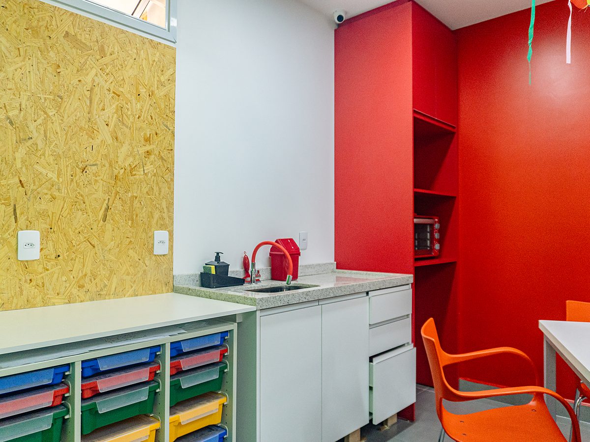 Sala criativa da unidade Taubaté, com bancada, pia, gaveteiros coloridos e parede vermelha