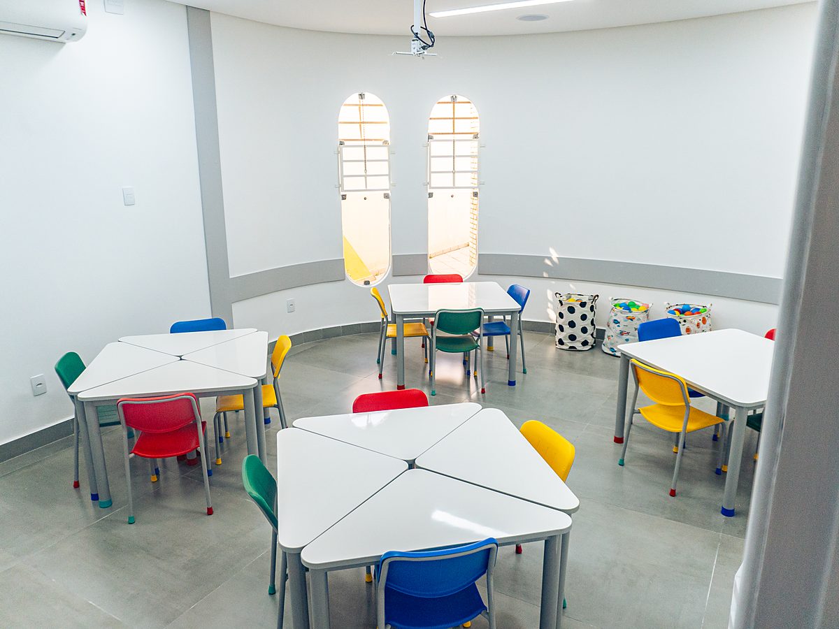 Sala das turmas infantis da unidade Taubaté, com mesas triangulares brancas e cadeiras coloridas